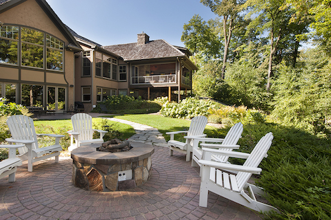 A patio with adirondack chairs, a curving fieldstone walk to the house