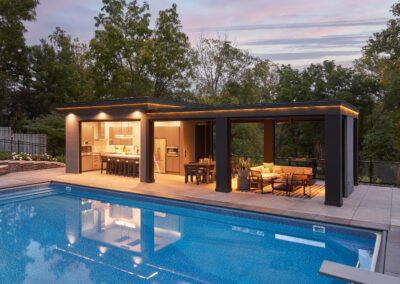 Outdoor in-ground pool with contemporary pool house featuring a bar/kitchen area and sitting area.