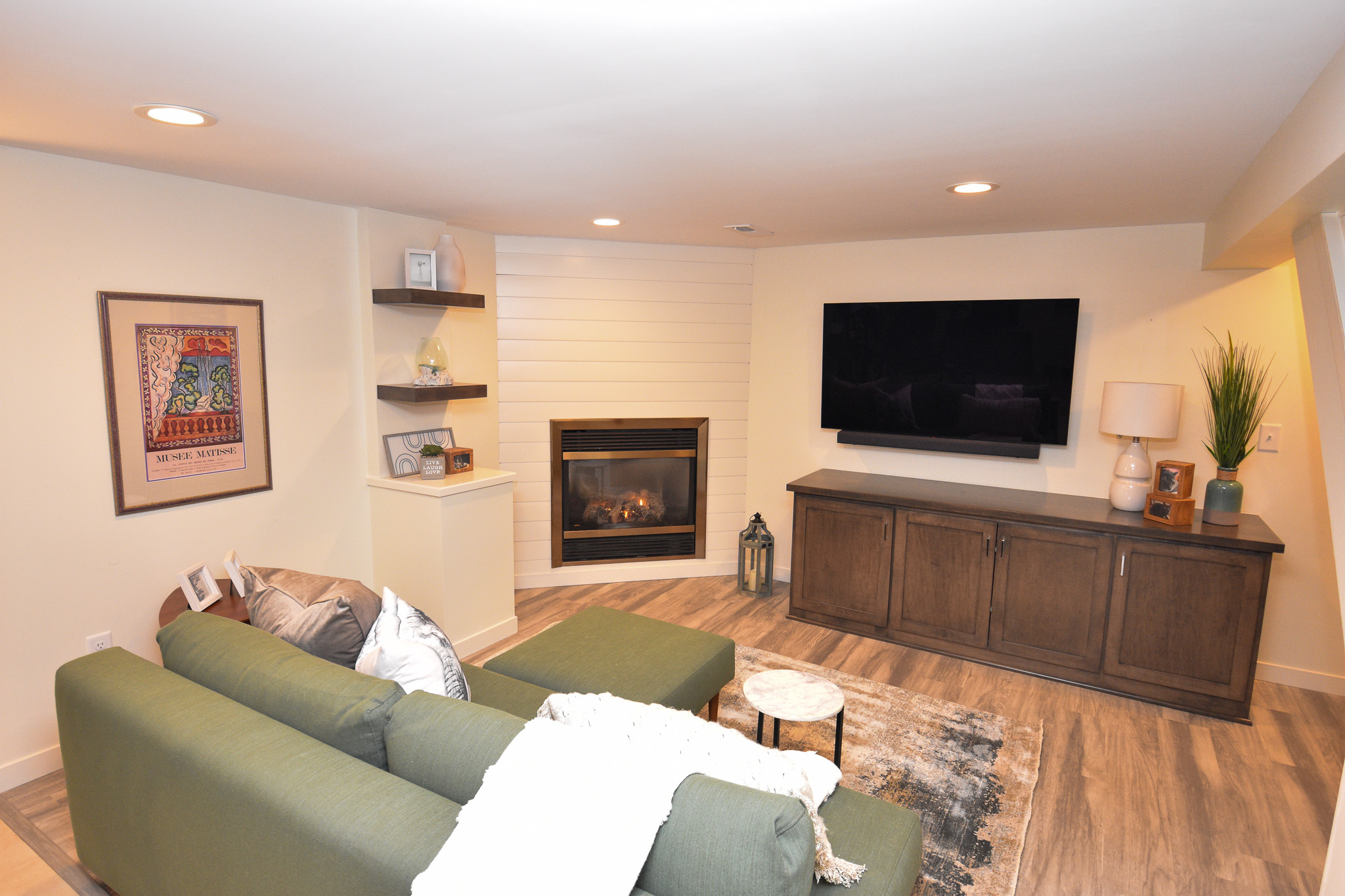 Basement remodel with white wood paneling, vinyl flooring, TV, fireplace